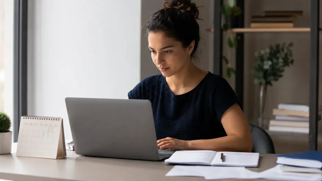 Estudante fazendo a inscrição do Enem 2026 pelo notebook, com documentos e calendário sobre a mesa.